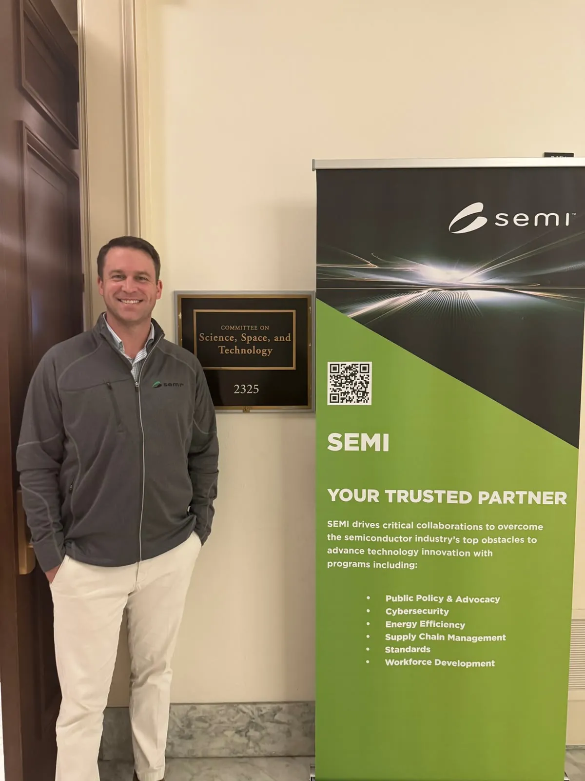 A TalentCraft team member beside a SEMI banner outside a House committee room.