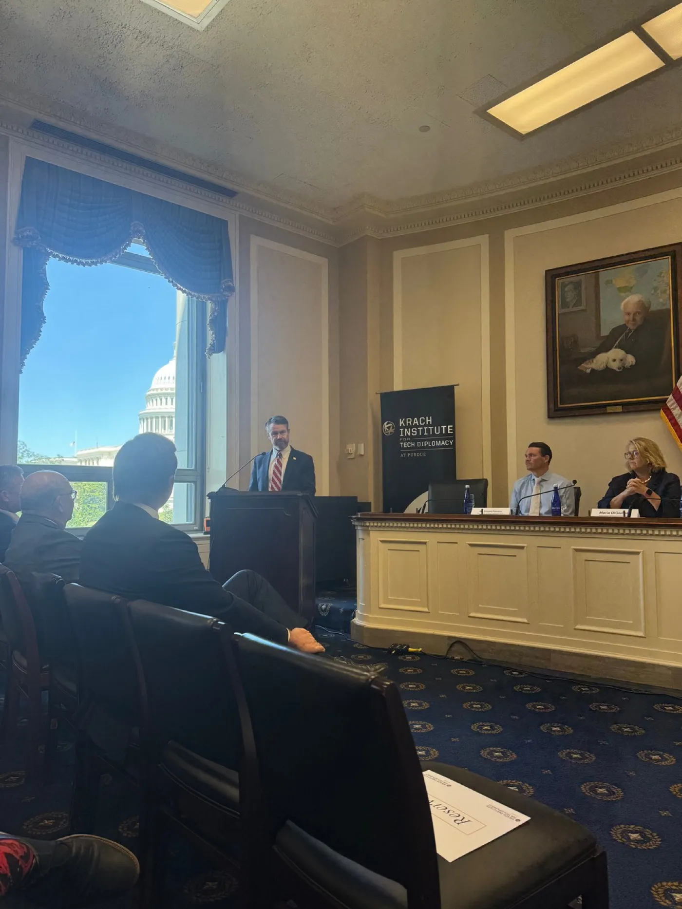 A Krach Institute session in the House Foreign Affairs Committee hearing room, the U.S. Capitol visible through the window.
